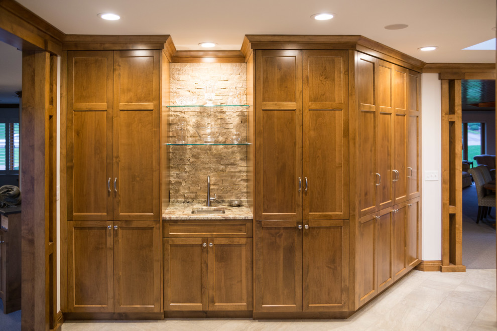 Design ideas for a mid-sized traditional single-wall wet bar in Minneapolis with an undermount sink, recessed-panel cabinets, medium wood cabinets, granite benchtops, beige splashback, stone tile splashback and travertine floors.