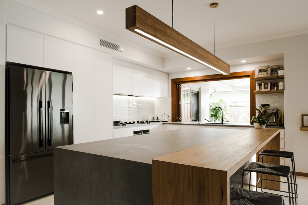 This is an example of a large modern l-shaped open plan kitchen in Sunshine Coast with a double-bowl sink, flat-panel cabinets, white cabinets, granite benchtops, white splashback, subway tile splashback, white appliances, porcelain floors, with island, beige floor, grey benchtop and recessed.