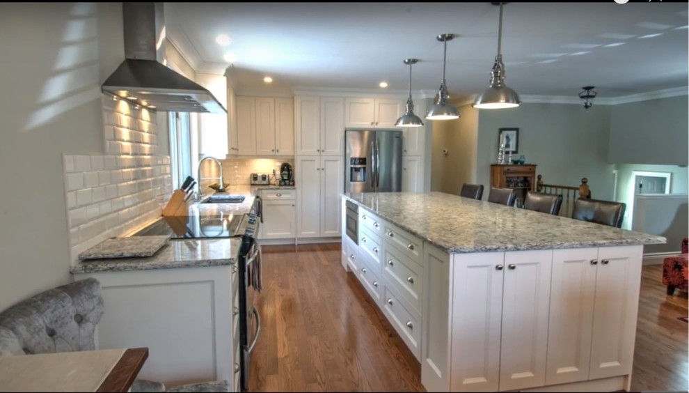Mid-sized transitional l-shaped medium tone wood floor and brown floor kitchen photo with an undermount sink, shaker cabinets, white cabinets, quartz countertops, white backsplash, subway tile backsplash, stainless steel appliances and an island