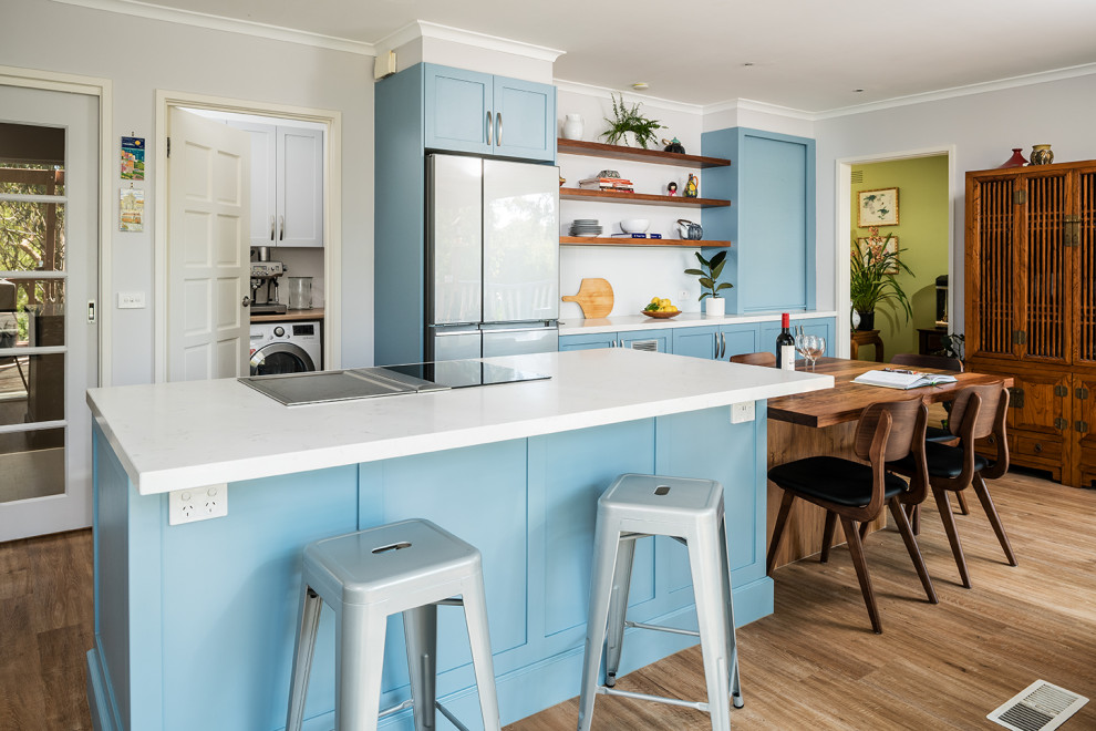 Inspiration for a large transitional eat-in kitchen in Melbourne with a double-bowl sink, shaker cabinets, blue cabinets, quartz benchtops, white splashback, glass sheet splashback, black appliances, medium hardwood floors, with island, brown floor and white benchtop.