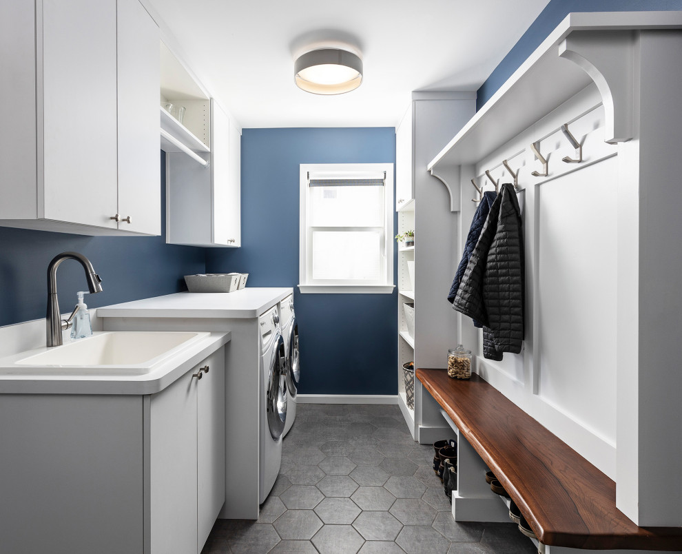 This is an example of a mid-sized transitional single-wall utility room in Detroit with a drop-in sink, flat-panel cabinets, white cabinets, blue walls, a side-by-side washer and dryer, brown floor and white benchtop.