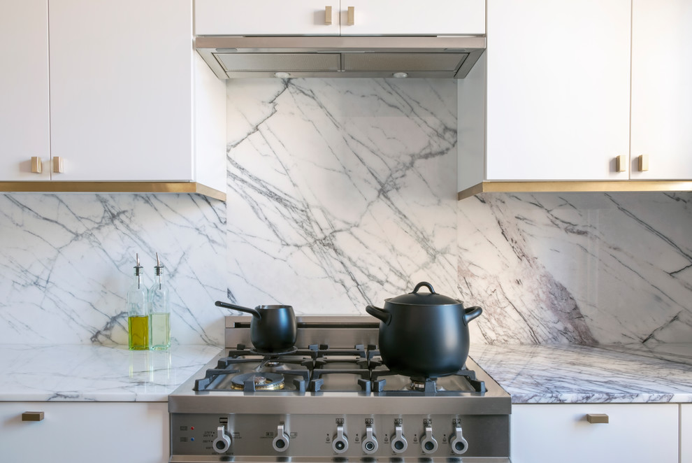 Example of a mid-sized trendy galley porcelain tile and gray floor open concept kitchen design in New York with a double-bowl sink, flat-panel cabinets, white cabinets, marble countertops, white backsplash, marble backsplash, stainless steel appliances and no island