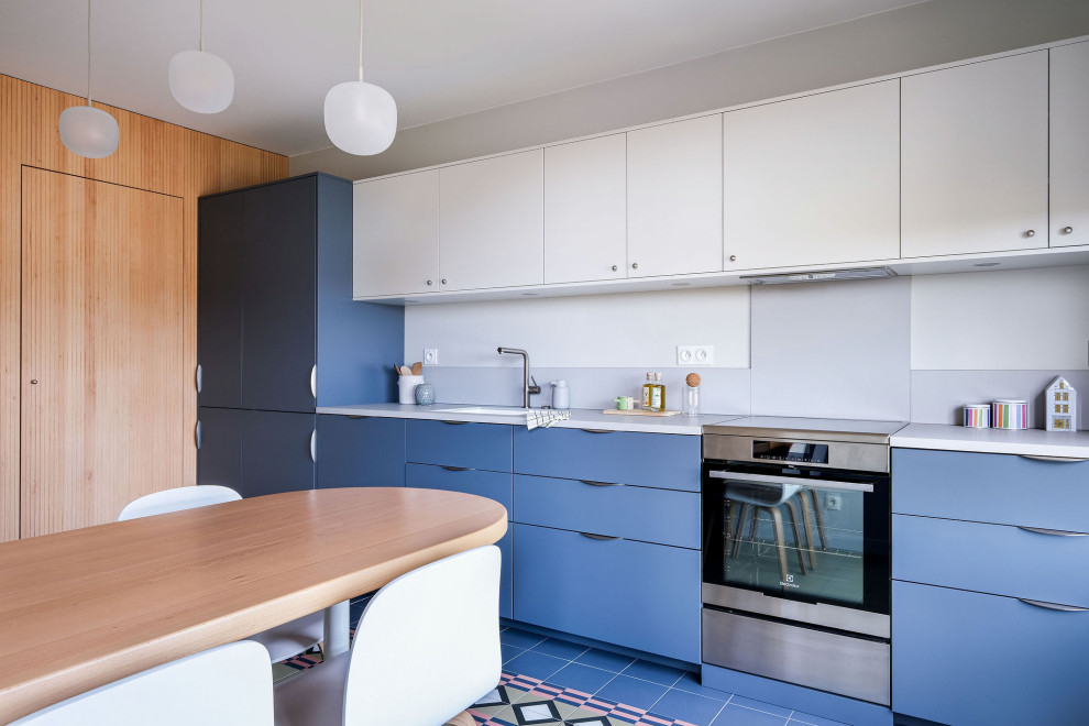 Idée de décoration pour une cuisine linéaire design de taille moyenne avec un placard à porte plane, des portes de placard bleues, carreaux de ciment au sol, un sol multicolore, un plan de travail gris et machine à laver.