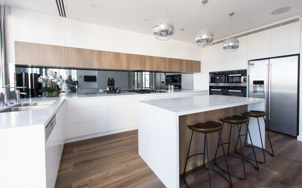 Design ideas for a large modern u-shaped open plan kitchen in Sydney with an undermount sink, flat-panel cabinets, white cabinets, marble benchtops, mirror splashback, stainless steel appliances, medium hardwood floors and with island.