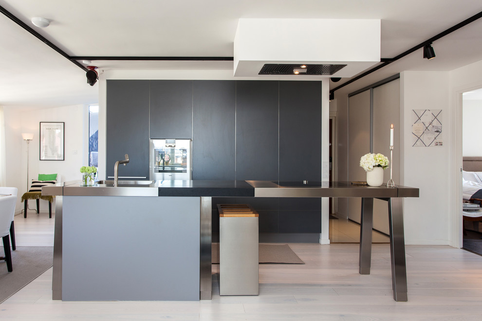 Design ideas for a large contemporary single-wall kitchen in Stockholm with an integrated sink, flat-panel cabinets, black cabinets, stainless steel benchtops, stainless steel appliances, light hardwood floors and with island.