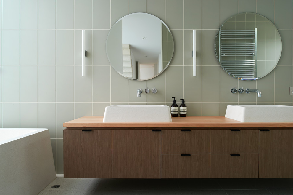Photo of a large contemporary master bathroom in Melbourne with a vessel sink, flat-panel cabinets, light wood cabinets, wood benchtops, a freestanding tub, porcelain tile, grey walls, marble floors and white tile.