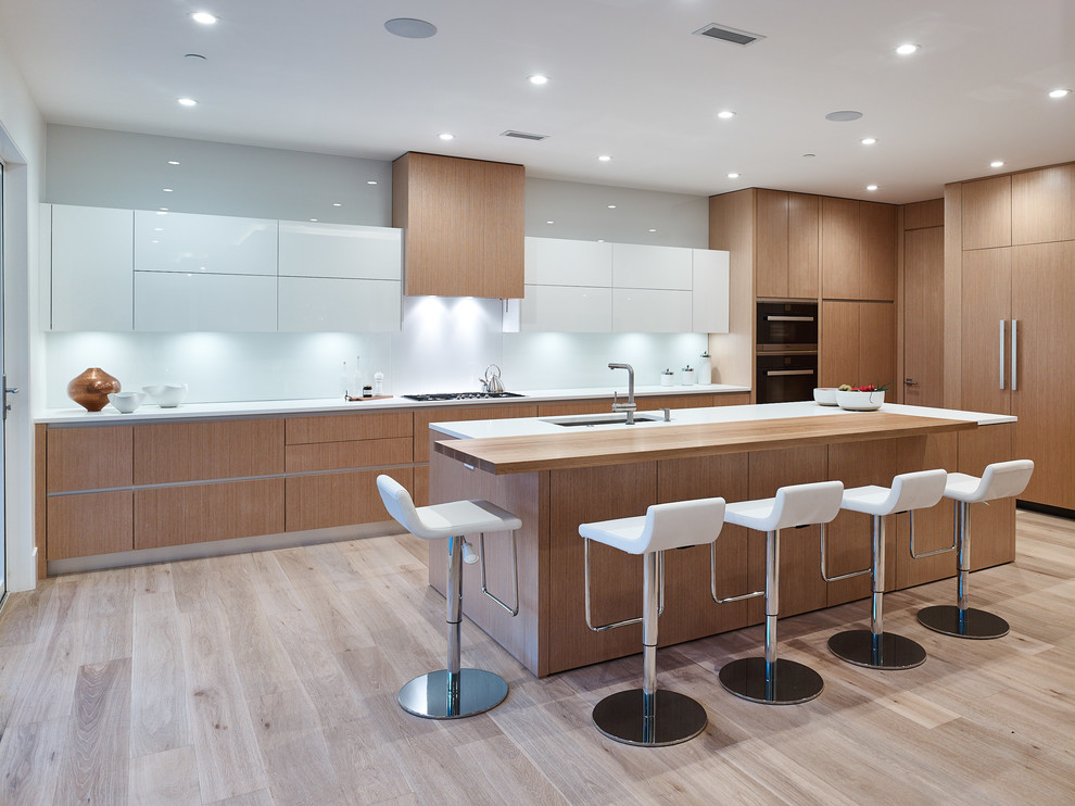 Photo of a large modern l-shaped open plan kitchen in Vancouver with an undermount sink, flat-panel cabinets, light wood cabinets, quartz benchtops, white splashback, panelled appliances, light hardwood floors, with island, beige floor and white benchtop.