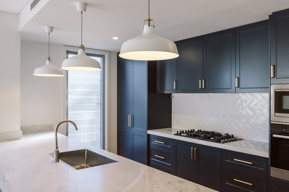 Inspiration for a mid-sized contemporary galley kitchen in Wollongong with a single-bowl sink, shaker cabinets, blue cabinets, marble benchtops, white splashback, ceramic splashback, stainless steel appliances, light hardwood floors, with island and grey benchtop.