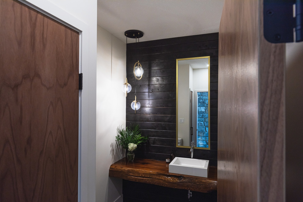 На фото: туалет среднего размера в стиле рустика с черной плиткой, черными стенами, настольной раковиной, столешницей из дерева, коричневой столешницей и подвесной тумбой с