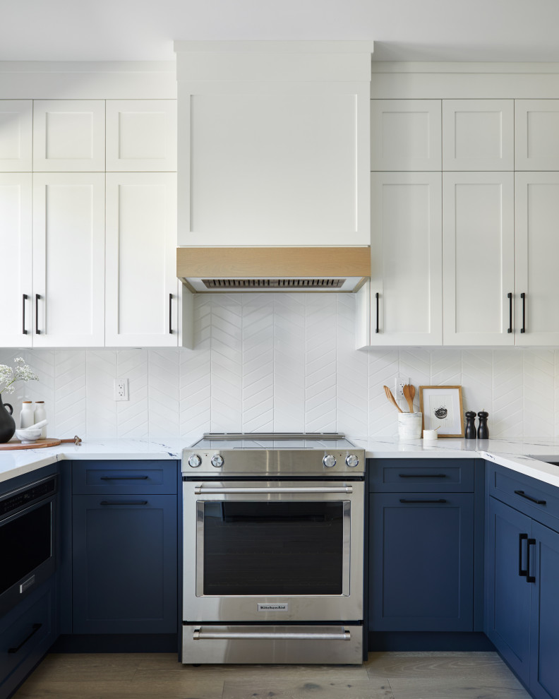 Inspiration for a mid-sized transitional u-shaped kitchen in Toronto with an undermount sink, shaker cabinets, blue cabinets, quartz benchtops, white splashback, ceramic splashback, stainless steel appliances, light hardwood floors, a peninsula, beige floor and white benchtop.