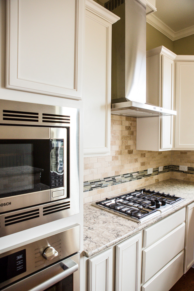 Example of a mid-sized transitional l-shaped medium tone wood floor eat-in kitchen design in Austin with an undermount sink, recessed-panel cabinets, white cabinets, granite countertops, beige backsplash, stone tile backsplash, stainless steel appliances and an island