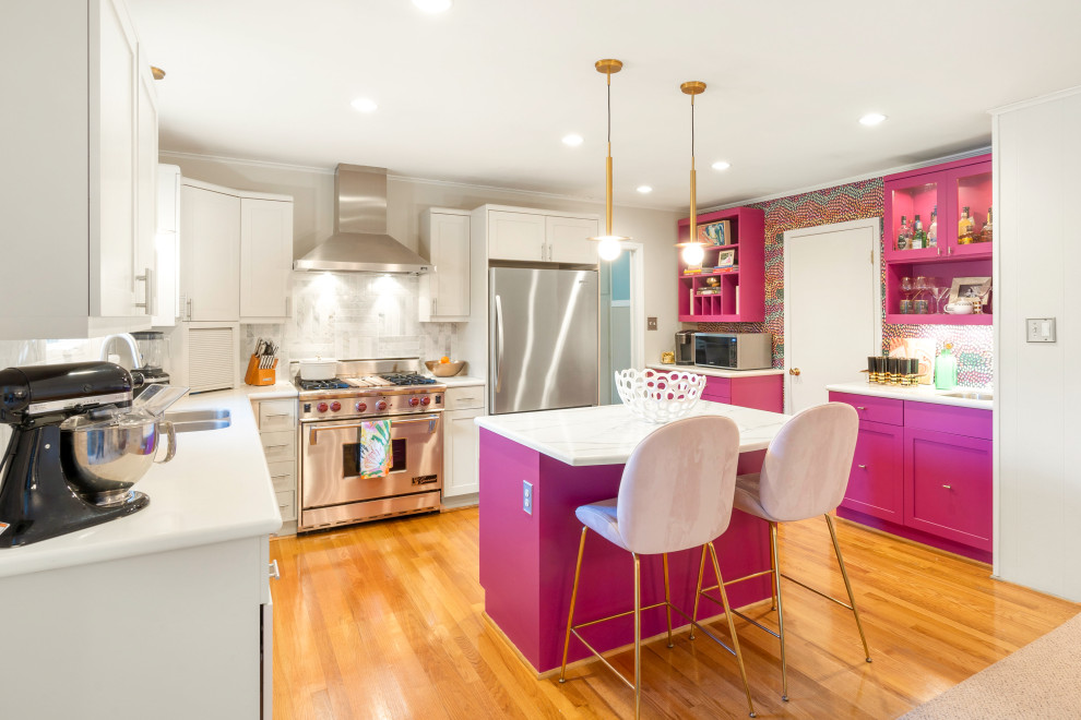 This is an example of a midcentury kitchen in Charlotte with shaker cabinets, pink cabinets, quartz benchtops, white splashback, marble splashback, stainless steel appliances, medium hardwood floors, with island, brown floor and white benchtop.