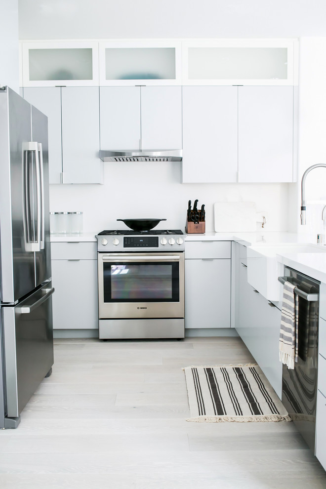 Design ideas for a small modern u-shaped eat-in kitchen in Los Angeles with a farmhouse sink, flat-panel cabinets, grey cabinets, quartz benchtops, white splashback, stone slab splashback, stainless steel appliances, light hardwood floors and a peninsula.