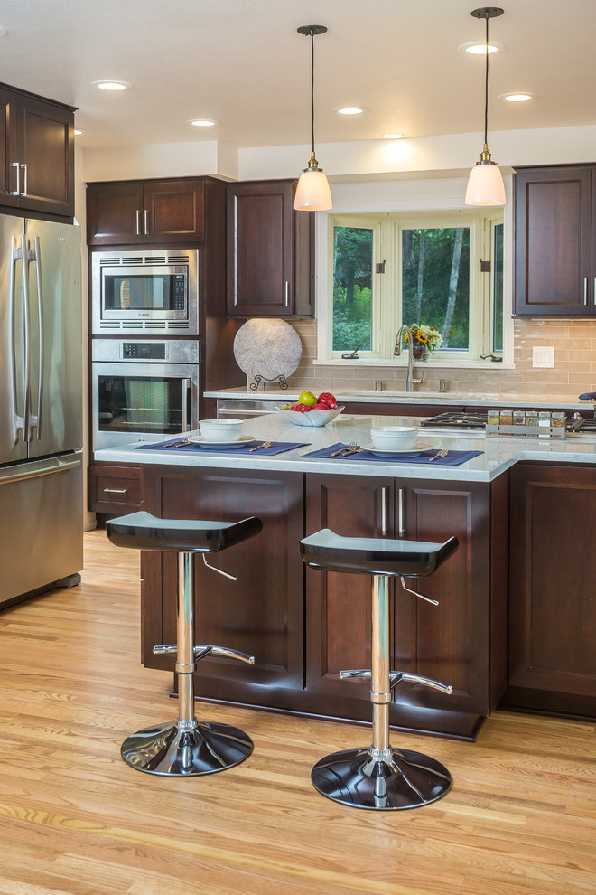 Mid-sized transitional l-shaped light wood floor open concept kitchen photo with an undermount sink, recessed-panel cabinets, dark wood cabinets, quartz countertops, gray backsplash, subway tile backsplash, stainless steel appliances and an island