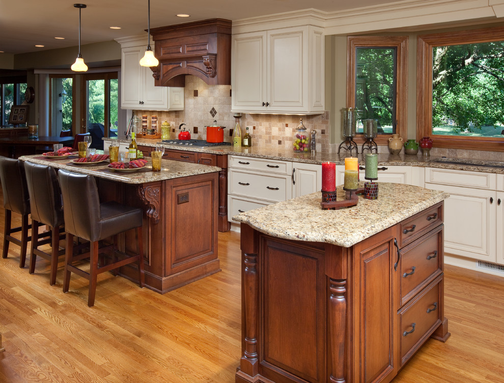 Design ideas for a large country l-shaped kitchen in Columbus with an undermount sink, raised-panel cabinets, beige cabinets, granite benchtops, beige splashback, stone tile splashback, panelled appliances, medium hardwood floors and multiple islands.