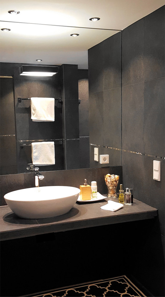 Inspiration for a large contemporary bathroom in Munich with a drop-in tub, an open shower, black tile, stone tile, black walls, ceramic floors, with a sauna, a vessel sink, black floor, open cabinets, black cabinets, a two-piece toilet, tile benchtops, an open shower and black benchtops.