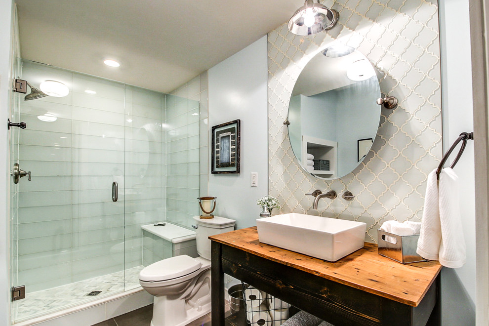 This is an example of a mid-sized eclectic master bathroom in Dallas with furniture-like cabinets, distressed cabinets, a freestanding tub, an alcove shower, a two-piece toilet, blue tile, glass tile, blue walls, porcelain floors, a vessel sink, wood benchtops, grey floor, a hinged shower door and brown benchtops.