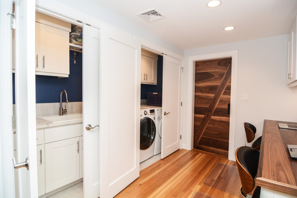 This is an example of a mid-sized contemporary single-wall utility room in Boston with a drop-in sink, recessed-panel cabinets, white cabinets, quartz benchtops, white splashback, engineered quartz splashback, blue walls, porcelain floors, a side-by-side washer and dryer, grey floor and white benchtop.