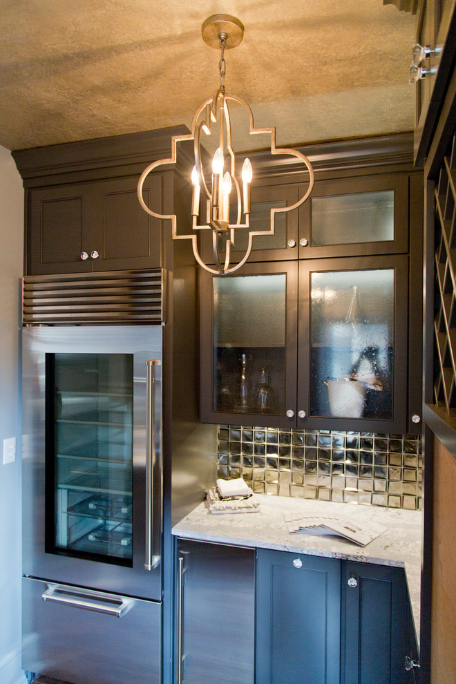 This is an example of a mid-sized transitional galley wet bar in Kansas City with glass-front cabinets, grey cabinets, granite benchtops, metal splashback, dark hardwood floors and brown floor.