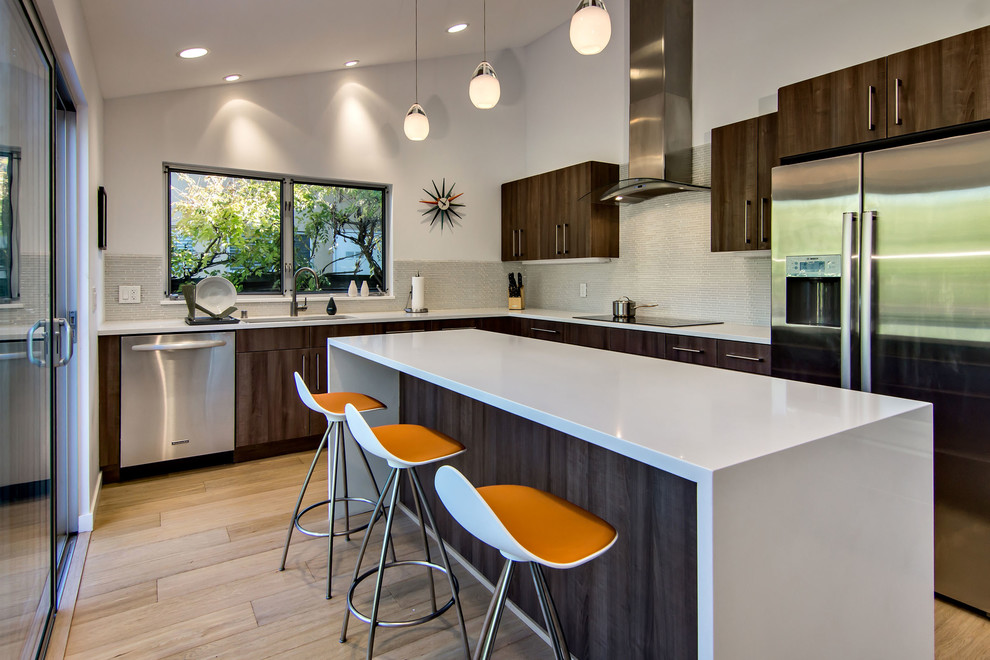 This is an example of a mid-sized midcentury l-shaped eat-in kitchen in San Francisco with an undermount sink, flat-panel cabinets, dark wood cabinets, quartz benchtops, grey splashback, glass tile splashback, stainless steel appliances, light hardwood floors, with island, brown floor and white benchtop.