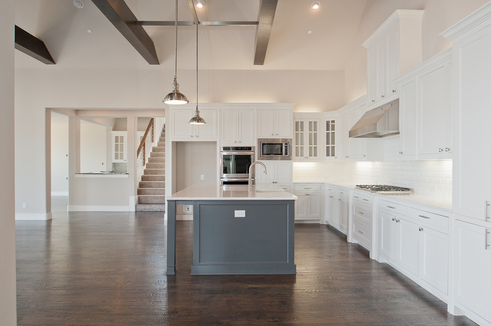 Design ideas for a large modern l-shaped open plan kitchen in Dallas with a farmhouse sink, shaker cabinets, white cabinets, granite benchtops, white splashback, subway tile splashback, stainless steel appliances, dark hardwood floors and with island.