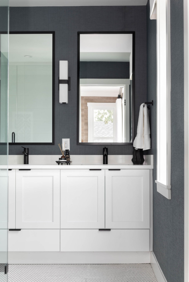 This is an example of a medium sized coastal ensuite bathroom in Vancouver with shaker cabinets, white cabinets, an alcove shower, a one-piece toilet, white tiles, cement tiles, blue walls, porcelain flooring, a submerged sink, quartz worktops, white floors, a hinged door, white worktops, double sinks, a built in vanity unit and wallpapered walls.