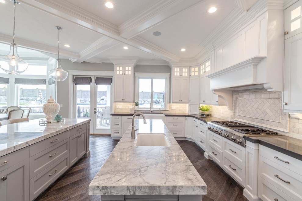 Large transitional u-shaped open plan kitchen in Salt Lake City with an undermount sink, recessed-panel cabinets, white cabinets, marble benchtops, white splashback, subway tile splashback, stainless steel appliances, medium hardwood floors, multiple islands and brown floor.