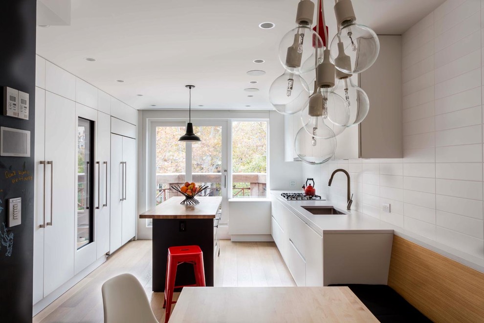 Mid-sized modern galley eat-in kitchen in New York with an undermount sink, flat-panel cabinets, white cabinets, solid surface benchtops, white splashback, ceramic splashback, stainless steel appliances, light hardwood floors and with island.