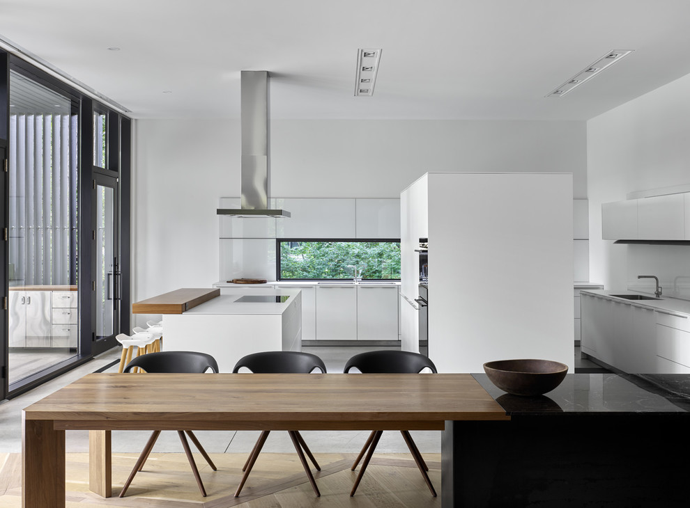 Inspiration for a large u-shaped open plan kitchen in Toronto with an undermount sink, flat-panel cabinets, white cabinets, window splashback, black appliances, concrete floors, with island and grey floor.