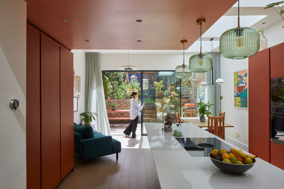 Große Moderne Wohnküche mit flächenbündigen Schrankfronten, roten Schränken, Granit-Arbeitsplatte, Korkboden, Kücheninsel, beigem Boden und weißer Arbeitsplatte in London
