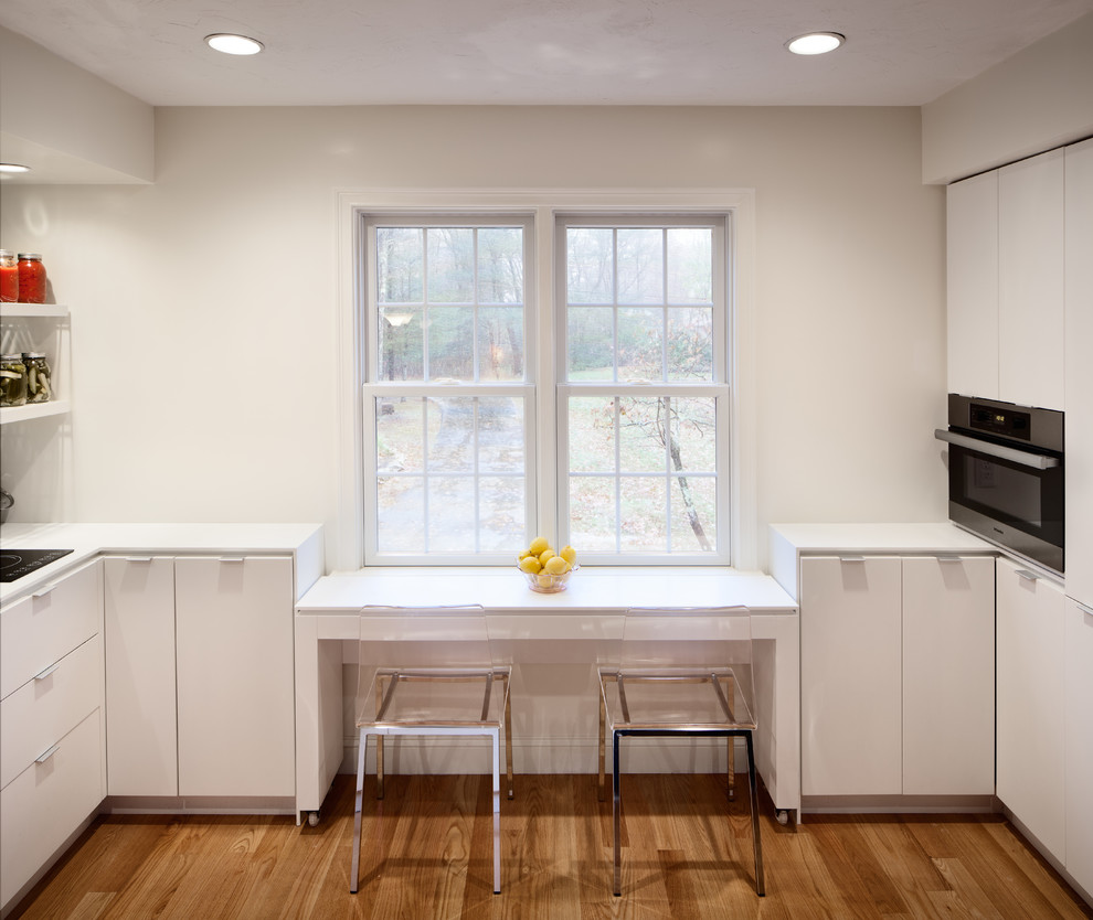 Photo of a contemporary u-shaped eat-in kitchen in Boston with stainless steel appliances, an undermount sink, flat-panel cabinets, white cabinets, solid surface benchtops and glass sheet splashback.