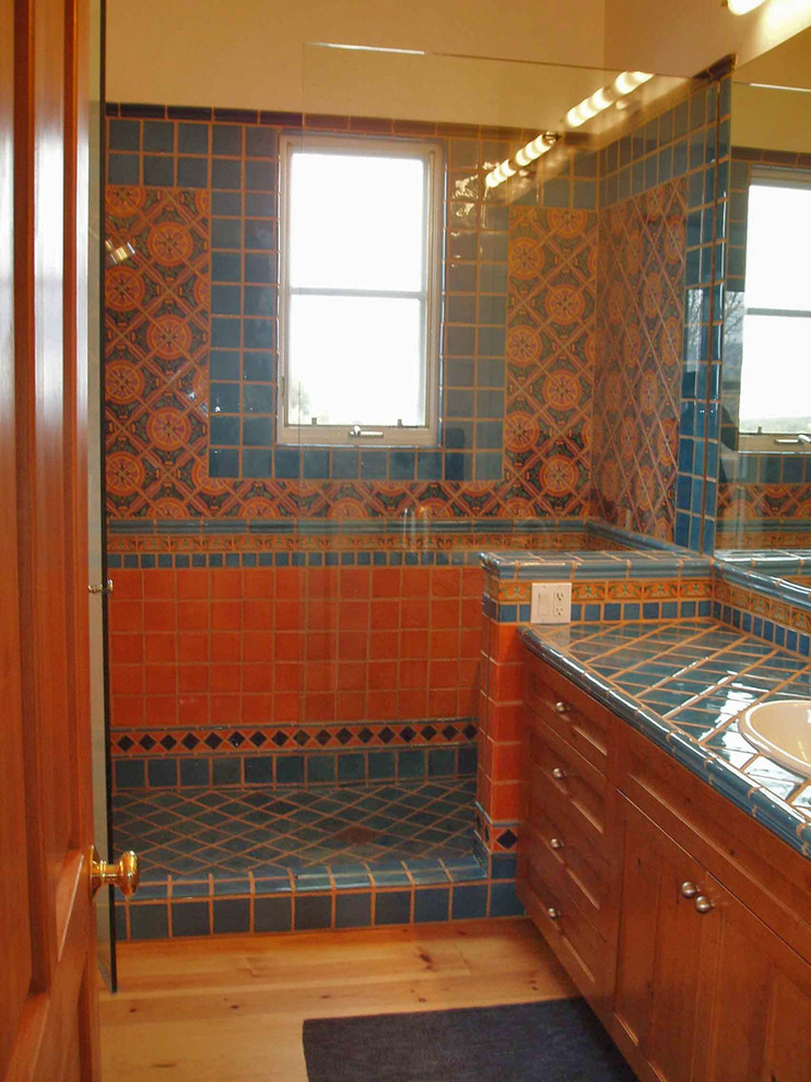 Inspiration for a mid-sized mediterranean bathroom in Albuquerque with a drop-in sink, shaker cabinets, medium wood cabinets, tile benchtops, multi-coloured tile, ceramic tile, beige walls and light hardwood floors.