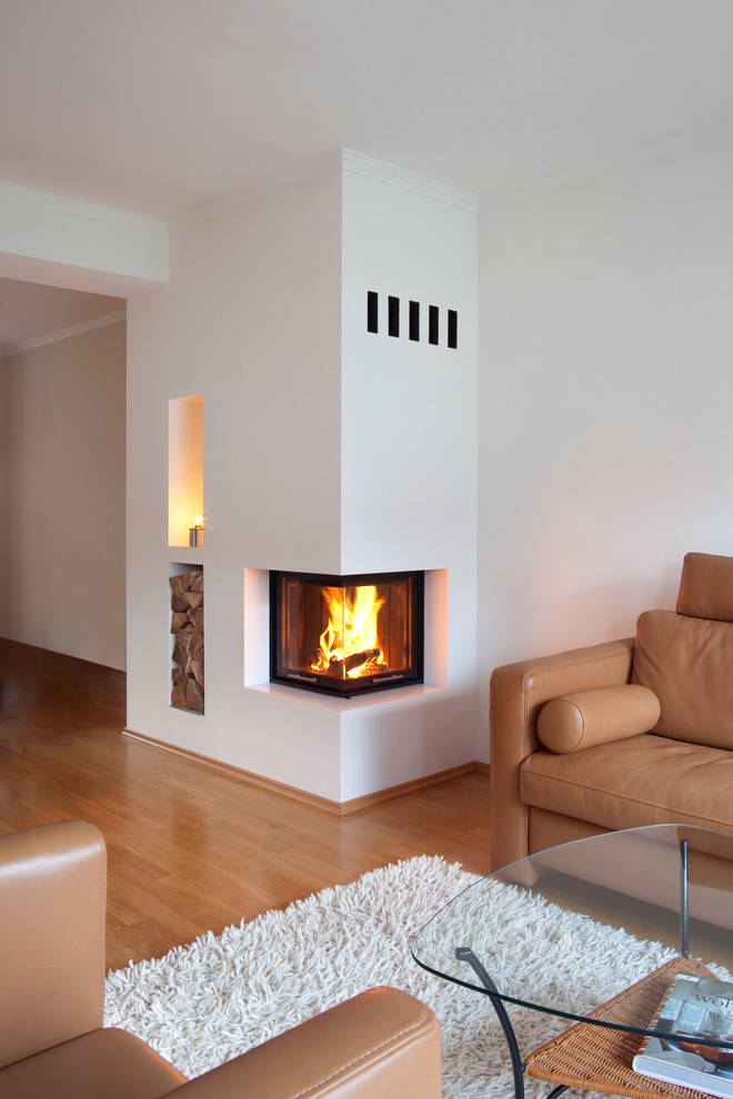 This is an example of a modern living room in Cologne with white walls, medium hardwood floors, a corner fireplace and a plaster fireplace surround.