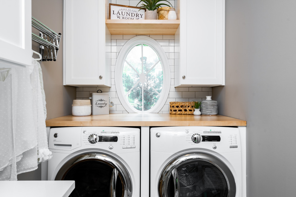 Inspiration for a small beach style single-wall utility room in St Louis with a drop-in sink, flat-panel cabinets, white cabinets, wood benchtops, white splashback, subway tile splashback, grey walls, porcelain floors, a side-by-side washer and dryer, grey floor and multi-coloured benchtop.