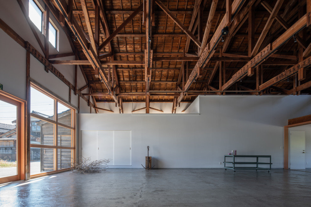 Cette photo montre un bureau industriel de taille moyenne et de type studio avec un mur blanc, sol en béton ciré, un sol gris et poutres apparentes.