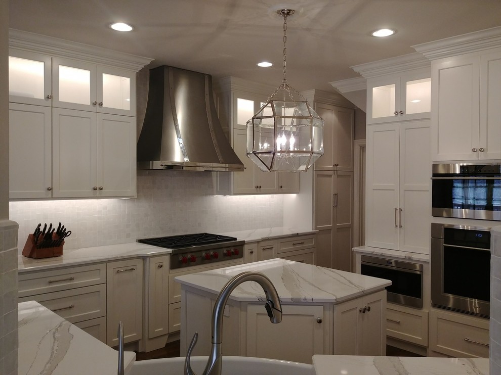 Enclosed kitchen - large transitional single-wall dark wood floor and brown floor enclosed kitchen idea in Nashville with a farmhouse sink, recessed-panel cabinets, white cabinets, quartzite countertops, white backsplash, subway tile backsplash, stainless steel appliances, an island and white countertops