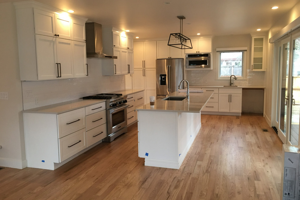 Kitchen - large l-shaped light wood floor and brown floor kitchen idea in Denver with a drop-in sink, shaker cabinets, white cabinets, granite countertops, white backsplash, an island and gray countertops