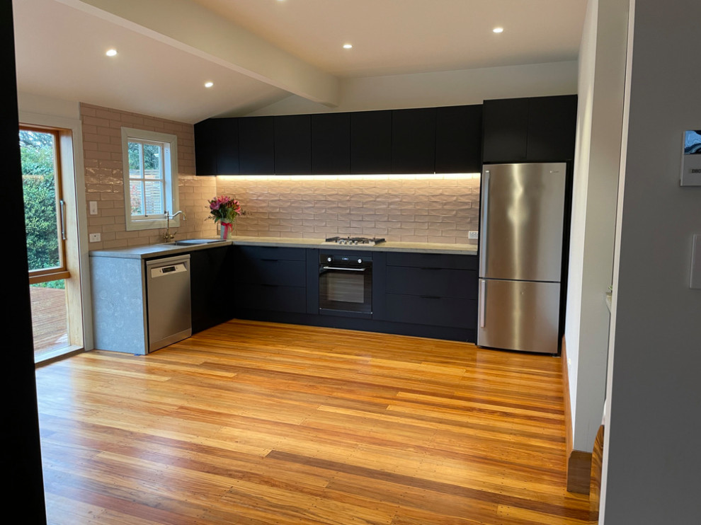 This is an example of a mid-sized modern l-shaped eat-in kitchen in Christchurch with a double-bowl sink, black cabinets, concrete benchtops, pink splashback, ceramic splashback, stainless steel appliances, light hardwood floors, no island and grey benchtop.
