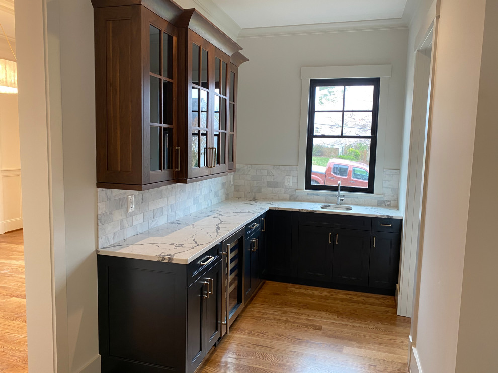 Photo of a mid-sized transitional l-shaped wet bar in DC Metro with an undermount sink, shaker cabinets, blue cabinets, quartz benchtops, grey splashback, marble splashback, medium hardwood floors, brown floor and white benchtop.