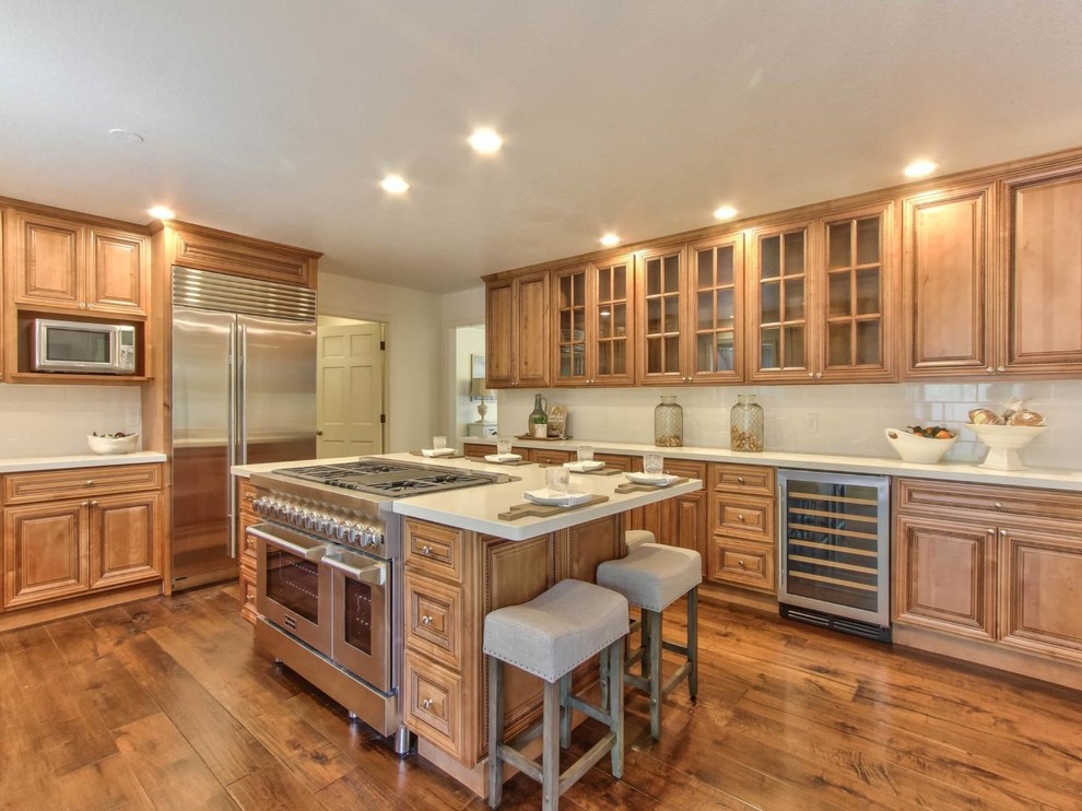 Example of a large transitional u-shaped medium tone wood floor kitchen design with an undermount sink, beaded inset cabinets, medium tone wood cabinets, quartz countertops, white backsplash, ceramic backsplash, stainless steel appliances, an island and white countertops