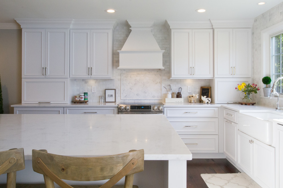 Photo of a traditional l-shaped kitchen in Detroit with a farmhouse sink, recessed-panel cabinets, white cabinets, white splashback, dark hardwood floors, with island and brown floor.