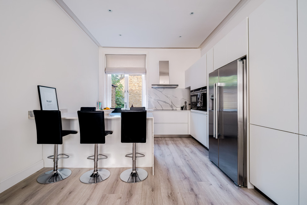 Photo of a mid-sized contemporary l-shaped open plan kitchen in London with an undermount sink, flat-panel cabinets, white cabinets, quartzite benchtops, white splashback, engineered quartz splashback, stainless steel appliances, laminate floors, a peninsula, grey floor, white benchtop and recessed.