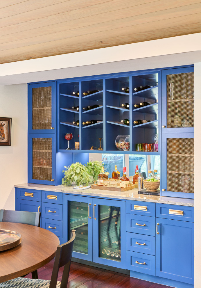 Inredning av en modern linjär hemmabar, med blå skåp, spegel som stänkskydd, luckor med infälld panel och mörkt trägolv