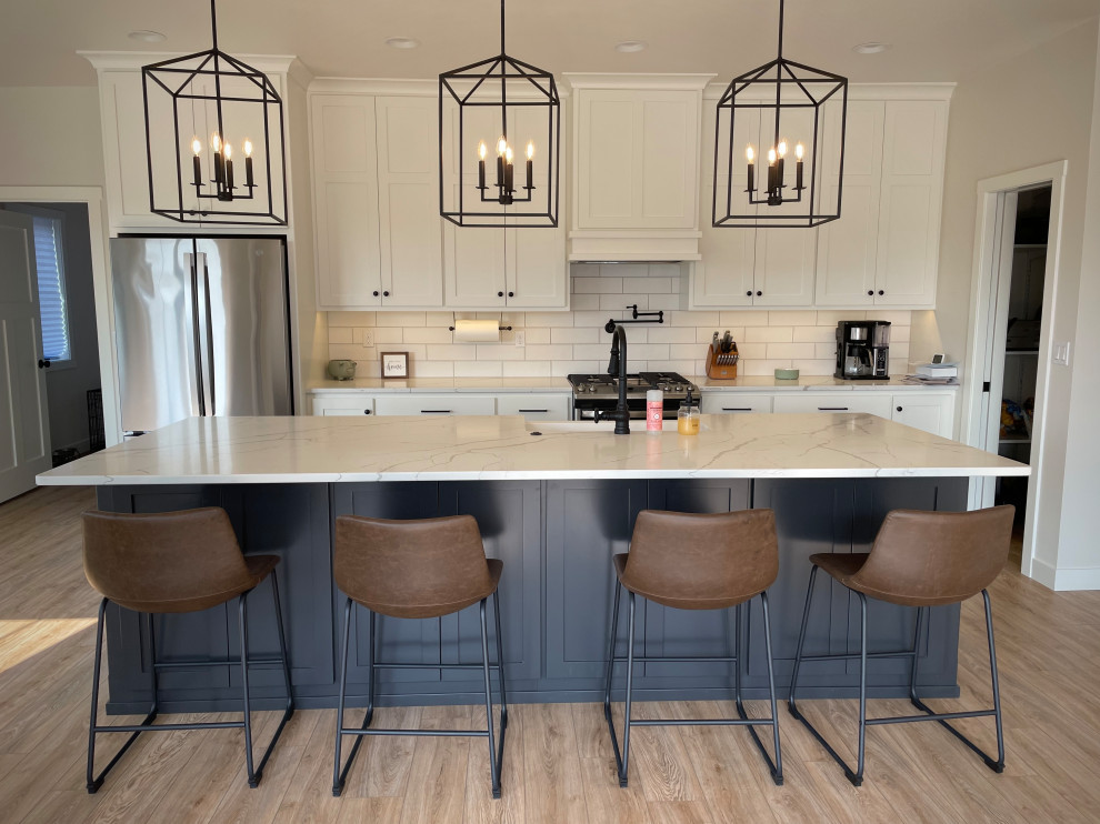 Inspiration for a light wood floor eat-in kitchen remodel with a farmhouse sink, shaker cabinets, white backsplash, subway tile backsplash, stainless steel appliances, an island and white countertops