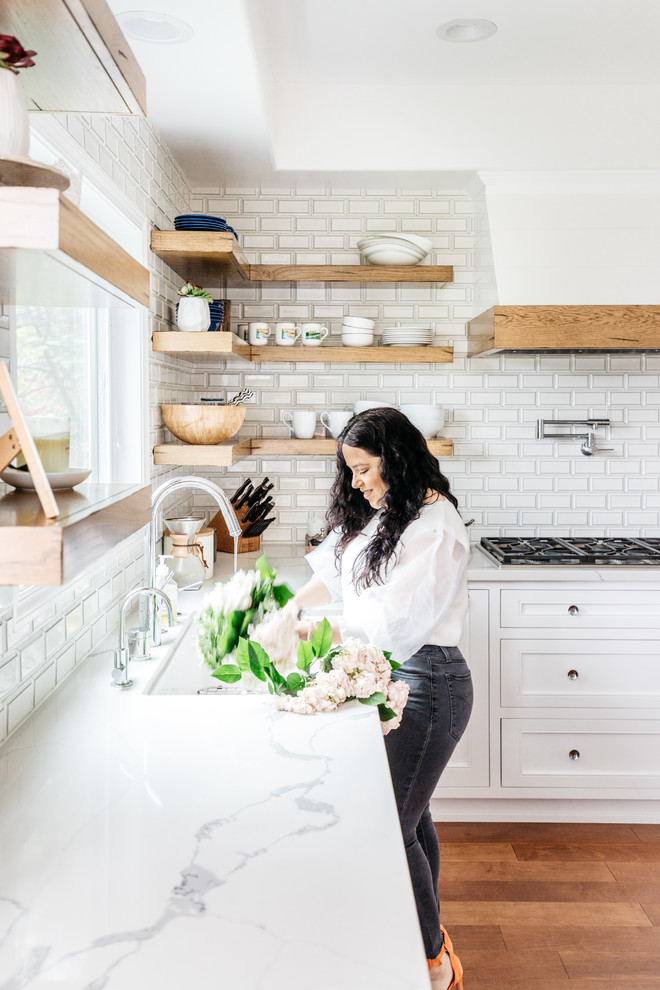 Eat-in kitchen - mid-sized transitional u-shaped medium tone wood floor and brown floor eat-in kitchen idea in Los Angeles with a farmhouse sink, recessed-panel cabinets, white cabinets, quartzite countertops, white backsplash, subway tile backsplash, stainless steel appliances, an island and white countertops
