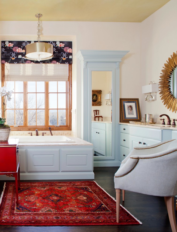 This is an example of a traditional bathroom in Denver with blue cabinets and a drop-in tub.