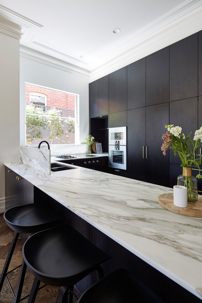 Inspiration for a mid-sized traditional u-shaped eat-in kitchen in Melbourne with a double-bowl sink, black cabinets, marble benchtops, multi-coloured splashback, marble splashback, stainless steel appliances, medium hardwood floors, with island, brown floor and multi-coloured benchtop.