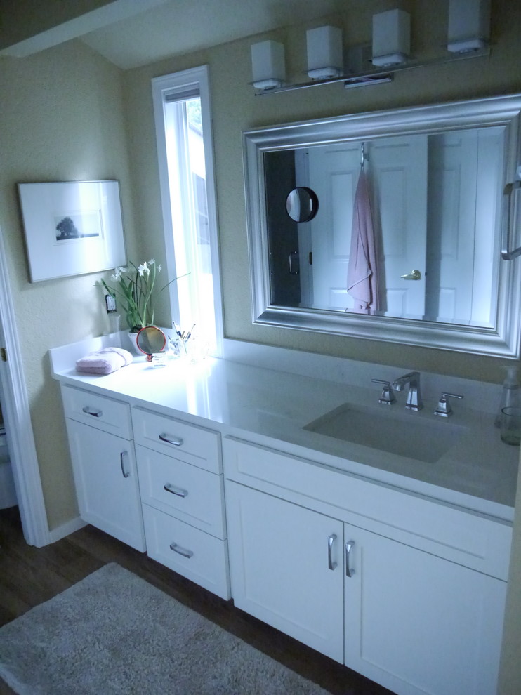 Photo of a large transitional master bathroom in Seattle with shaker cabinets, white cabinets, an alcove shower, a two-piece toilet, white tile, ceramic tile, yellow walls, vinyl floors, an undermount sink, engineered quartz benchtops, brown floor, a hinged shower door and white benchtops.