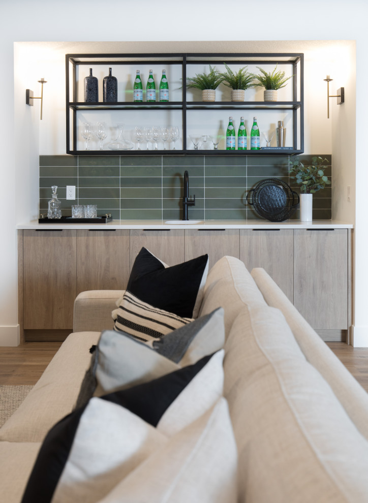 This is an example of a large transitional single-wall wet bar in Calgary with an undermount sink, flat-panel cabinets, light wood cabinets, solid surface benchtops, green splashback, porcelain splashback, vinyl floors, multi-coloured floor and white benchtop.