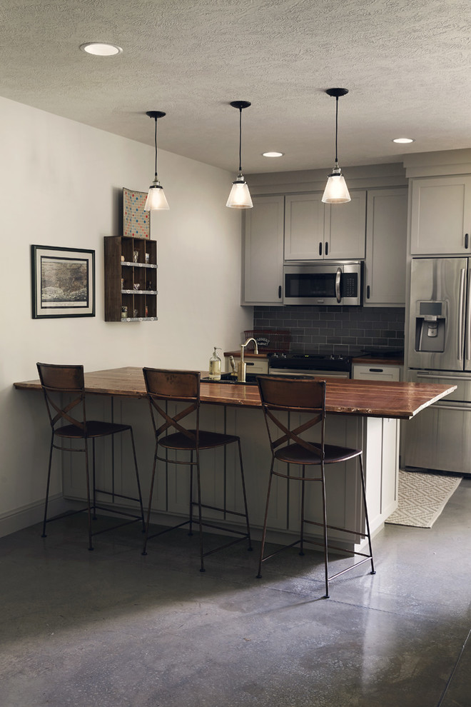 Inspiration for a small rustic galley concrete floor and gray floor eat-in kitchen remodel with a drop-in sink, shaker cabinets, white cabinets, wood countertops, white backsplash, subway tile backsplash, stainless steel appliances and brown countertops